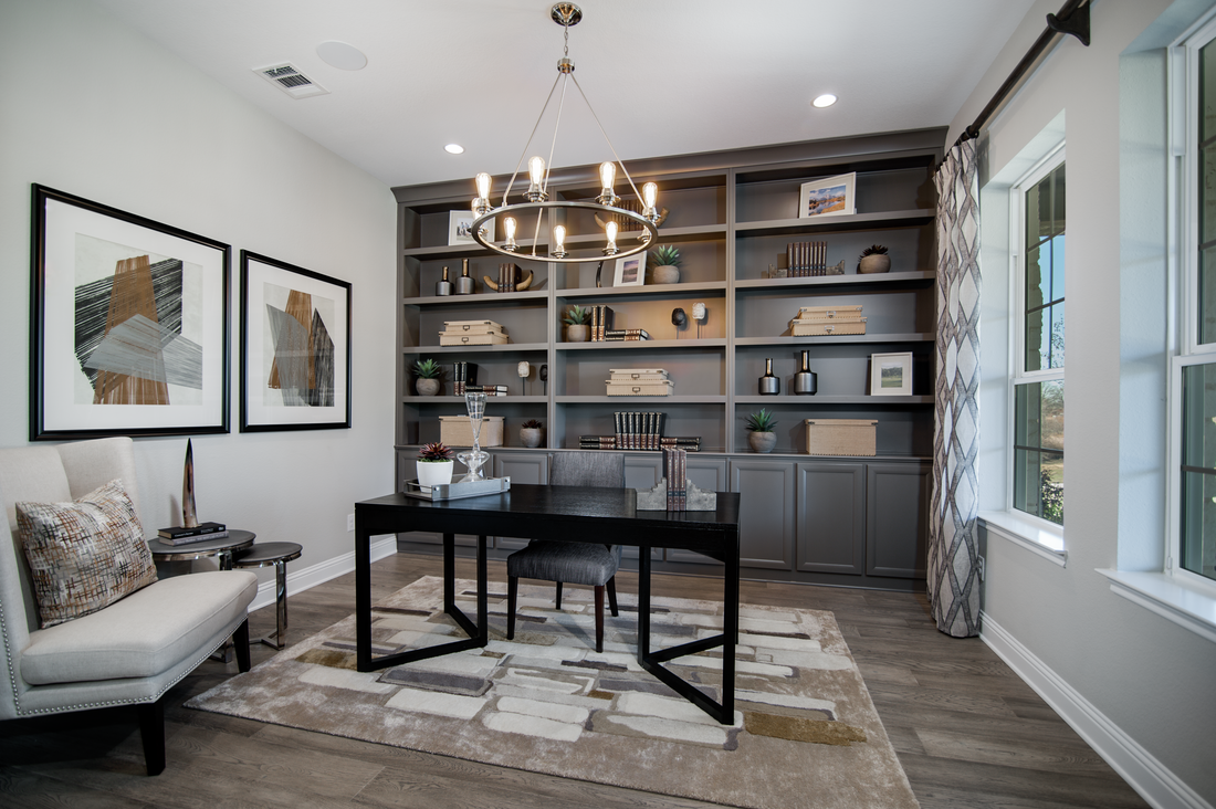 Large office with built-in bookself, black desk, hardwood floor and chandelier. 