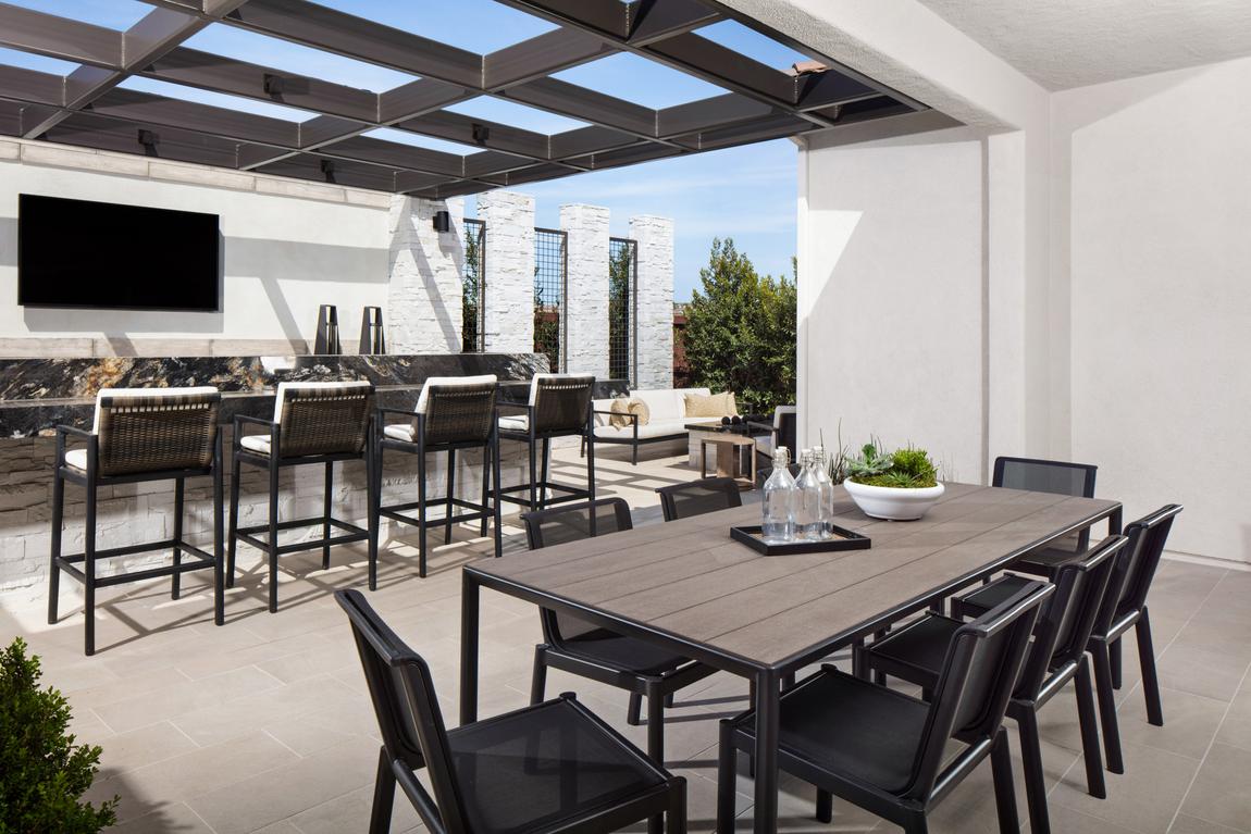 Outdoor living area with dining table and black chairs and bar with barstools under pergola