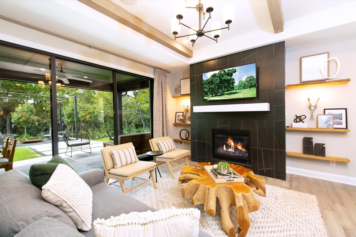 Living room with black accented fireplace, indoor to outdoor living entrance and artistic wood table. 