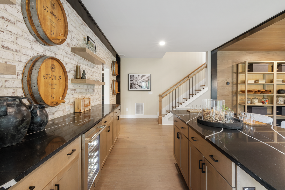 Bar with island, black countertops, wooden barrels adorning the stone wall and light brown flooring